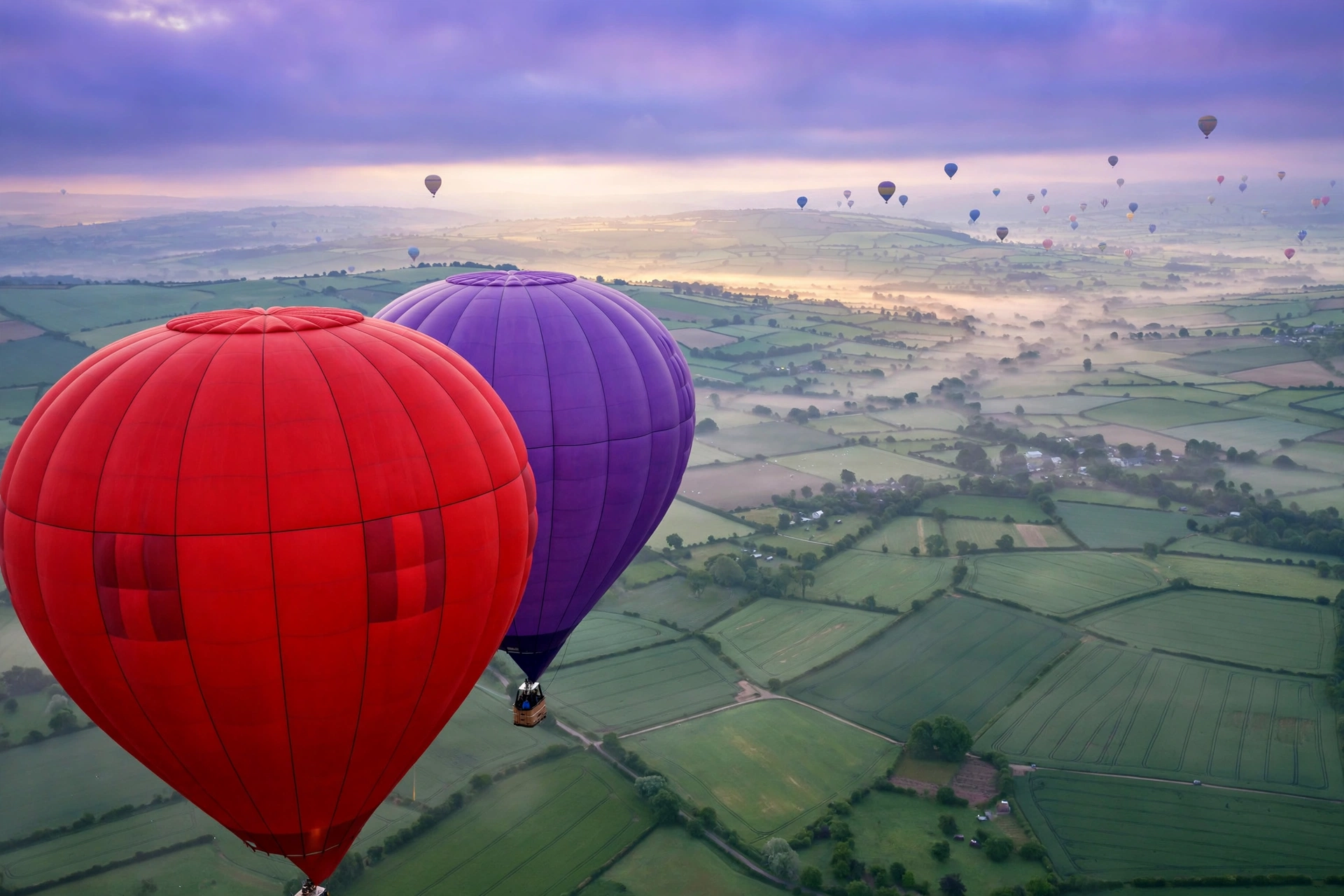 Hot-air balloons at dawn in scarlet, violet and green against a pale morning sky